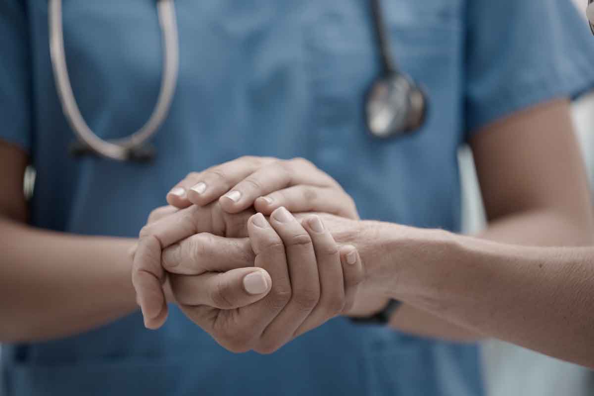 Close up af en læge som holder en patient hænder i sine egen, på en trøstende måde.