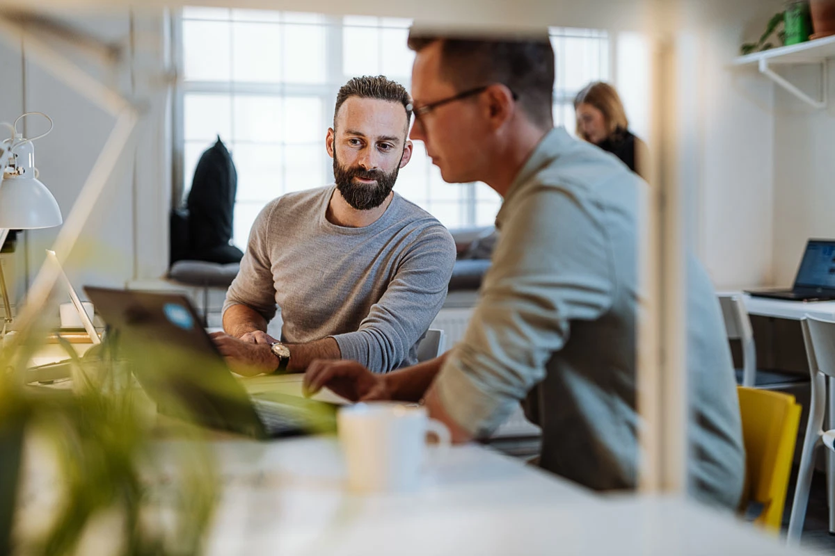 En mand kigger på en anden mands computer på et kontor.