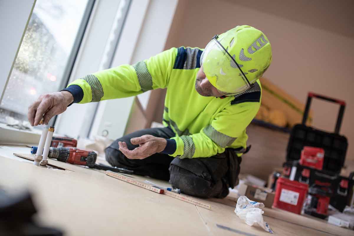 Håndværker sidder på sine knæ og arbejder på en radiator.
