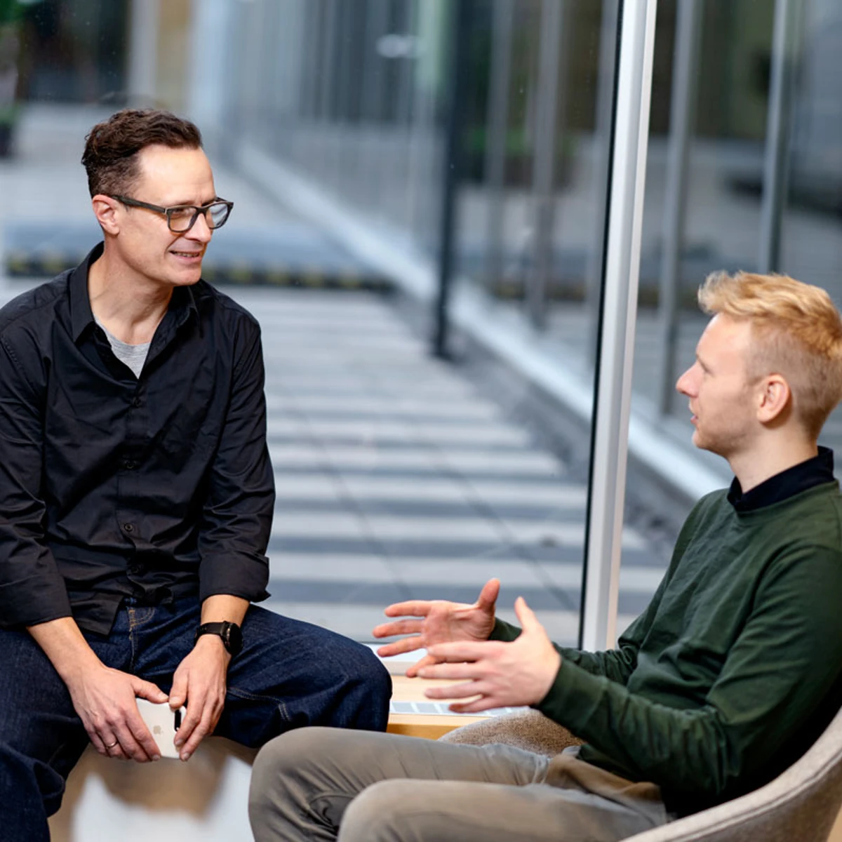 2 mænd sidder og snakker samme på et kontor.