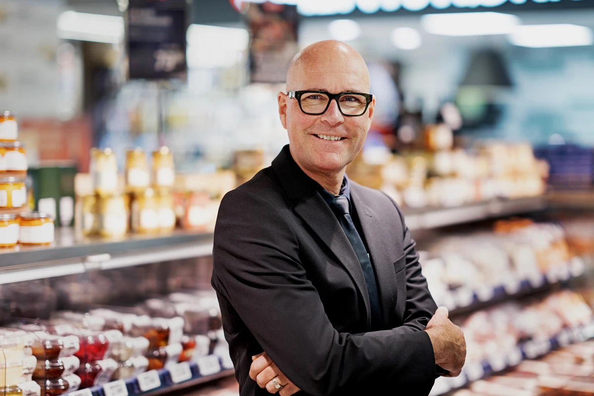 Portræt af købmand i Meny, der smiler til kameraet.