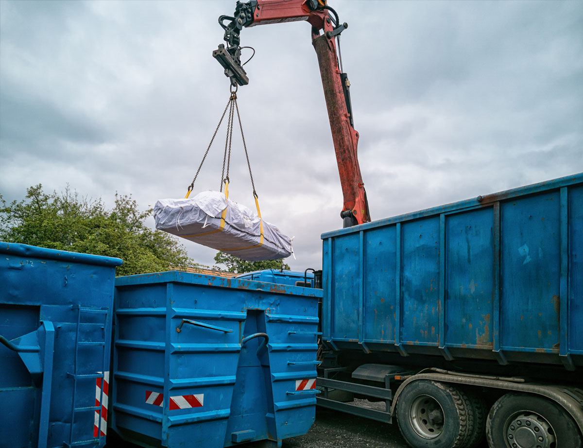 En kran hejser plastikindkapslet materiale ned i en container.