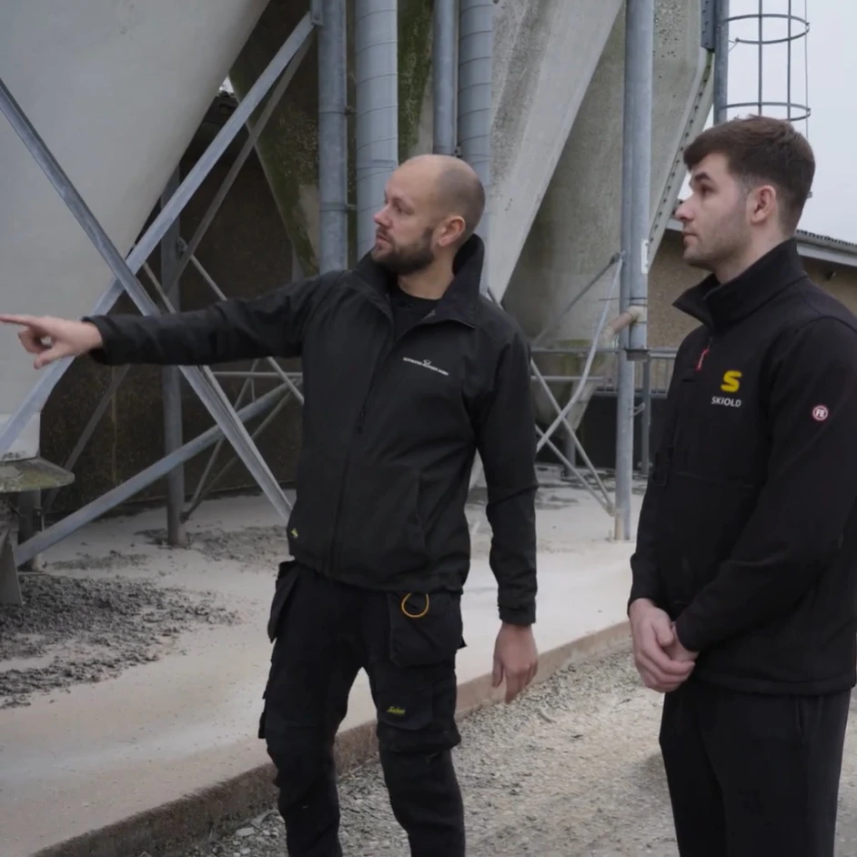 To mænd står ved fodersilo og snakker sammen.