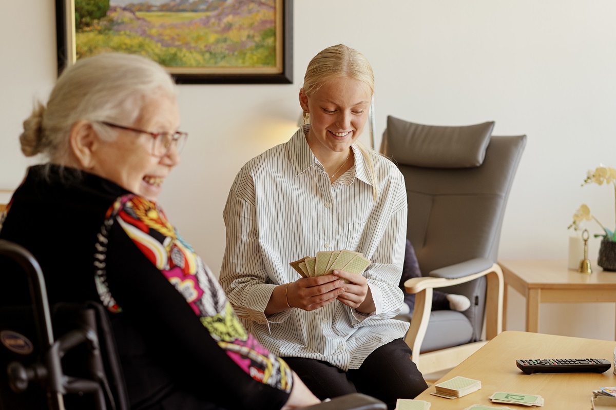 Ung Medarbjeder På Plejehjem Spiller Kort Med En Ældre Kvinde
