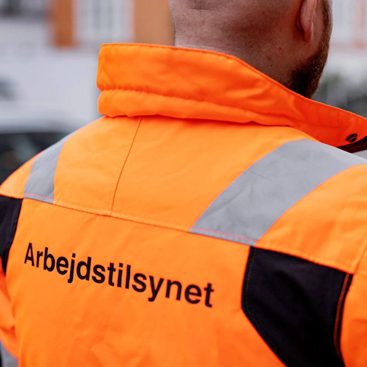 Ryggen af en tilsynsførende med en orange jakke på, hvor Arbejdstilsynets logo er på.