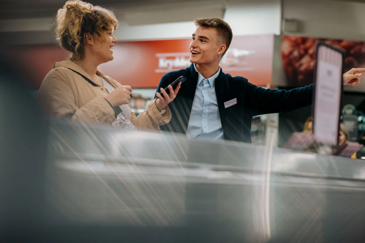 Supermarkedsansat står og snakker med en kunde i butikken.
