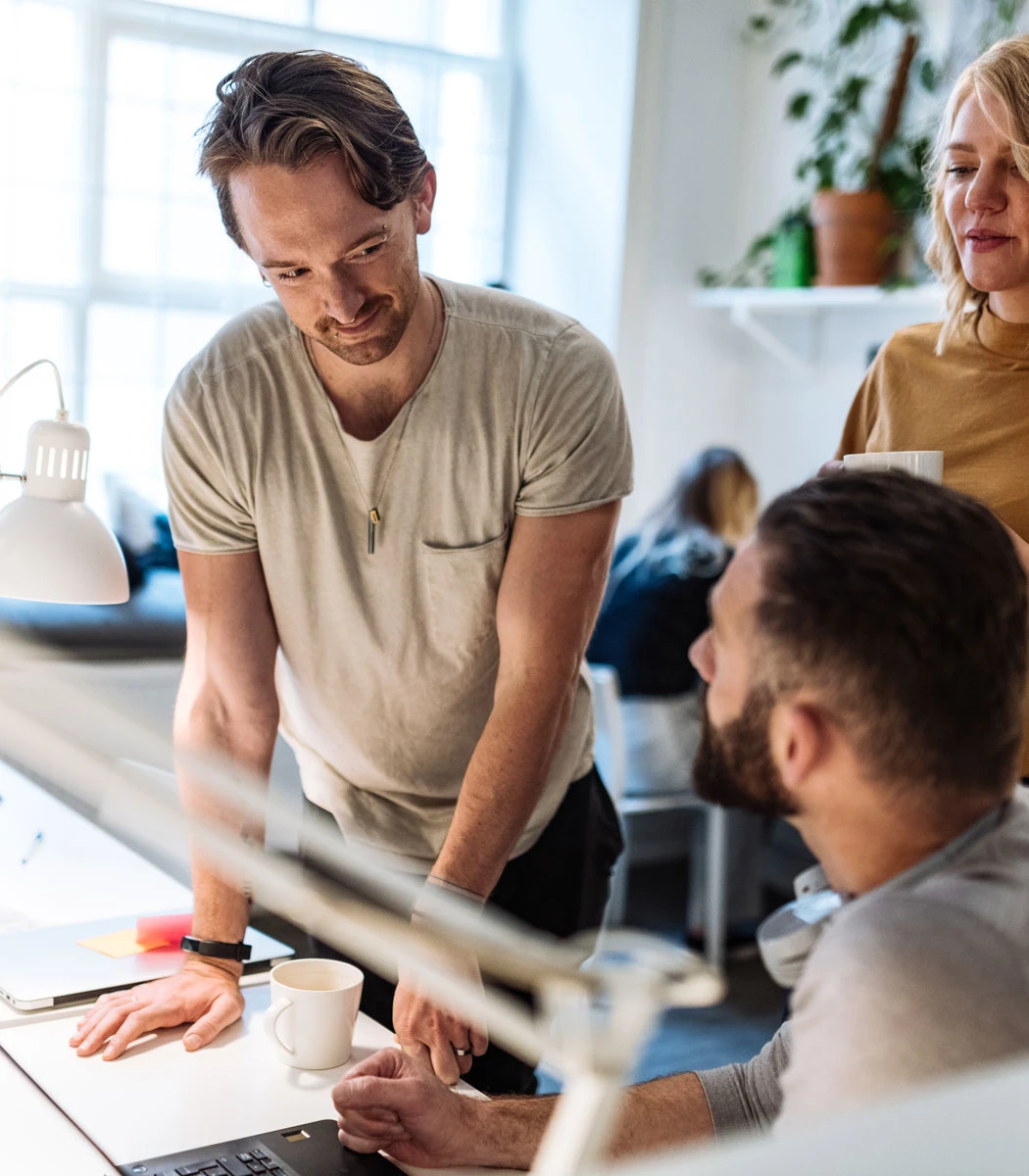 Mand læner sig op ad skrivebord og taler med kollega