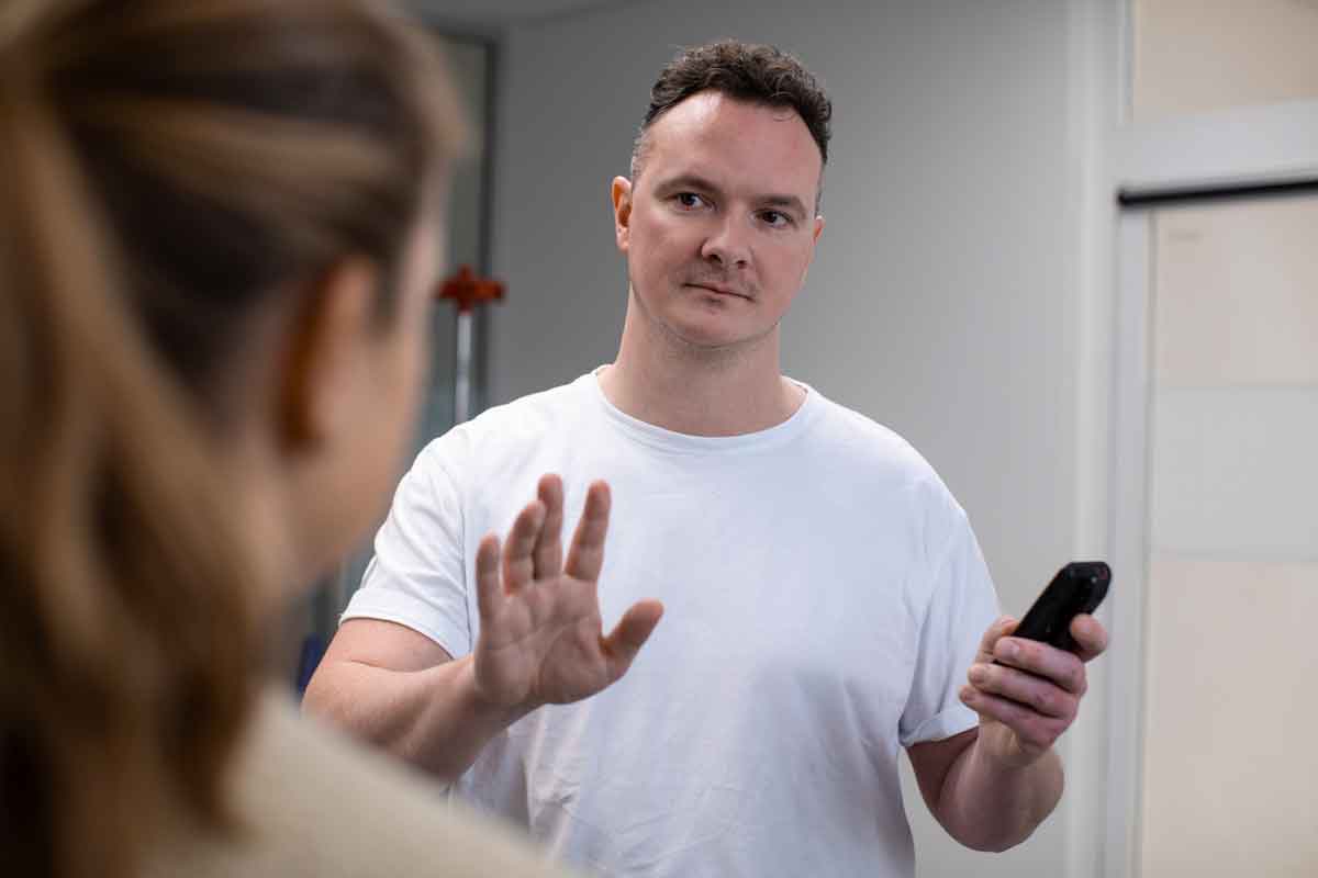 Hospitalsmedarbejder holder telefon og afviser en person som står foran ham.