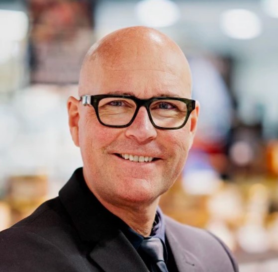 Portræt tæt på af købmand i Meny, der smiler til kameraet.