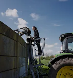 Landbrugsmedarbejder står i lift og kigger på silo med gylle
