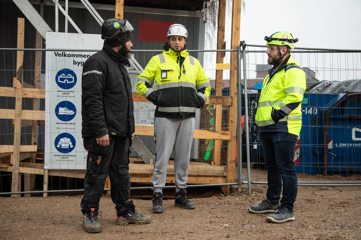 Tre håndværkere står og snakker på en byggeplads
