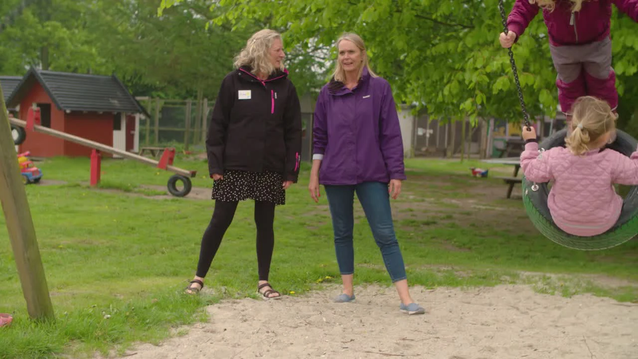To kvindelige pædagoger står og snakker på legeplads.