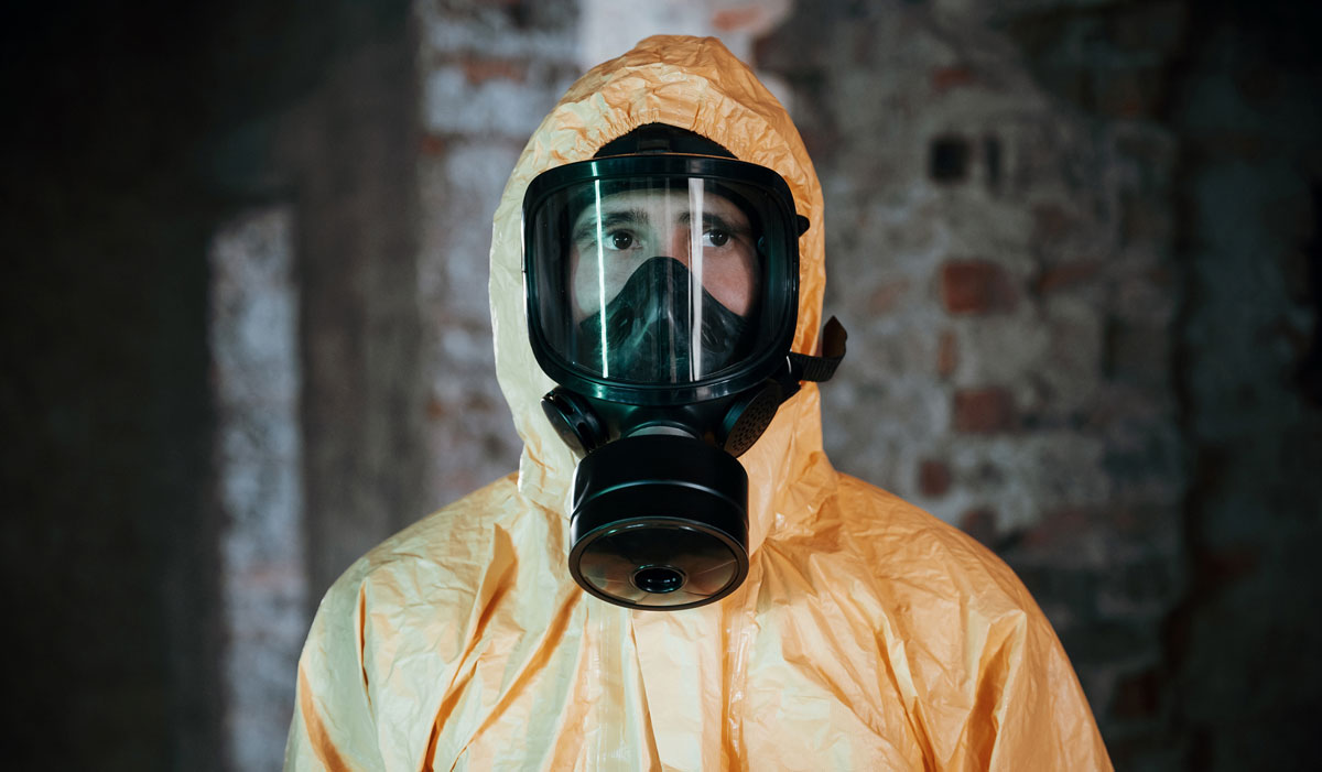 Person står med maske og beskyttelsesdragt på.