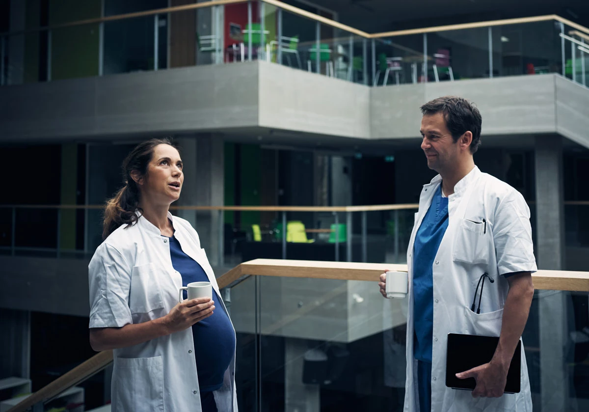 To kollegaer står og snakker på et hospital. En af dem er gravid.