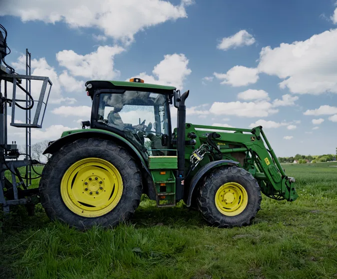 Grøn traktor på grøn mark og blå himmel i baggrunden